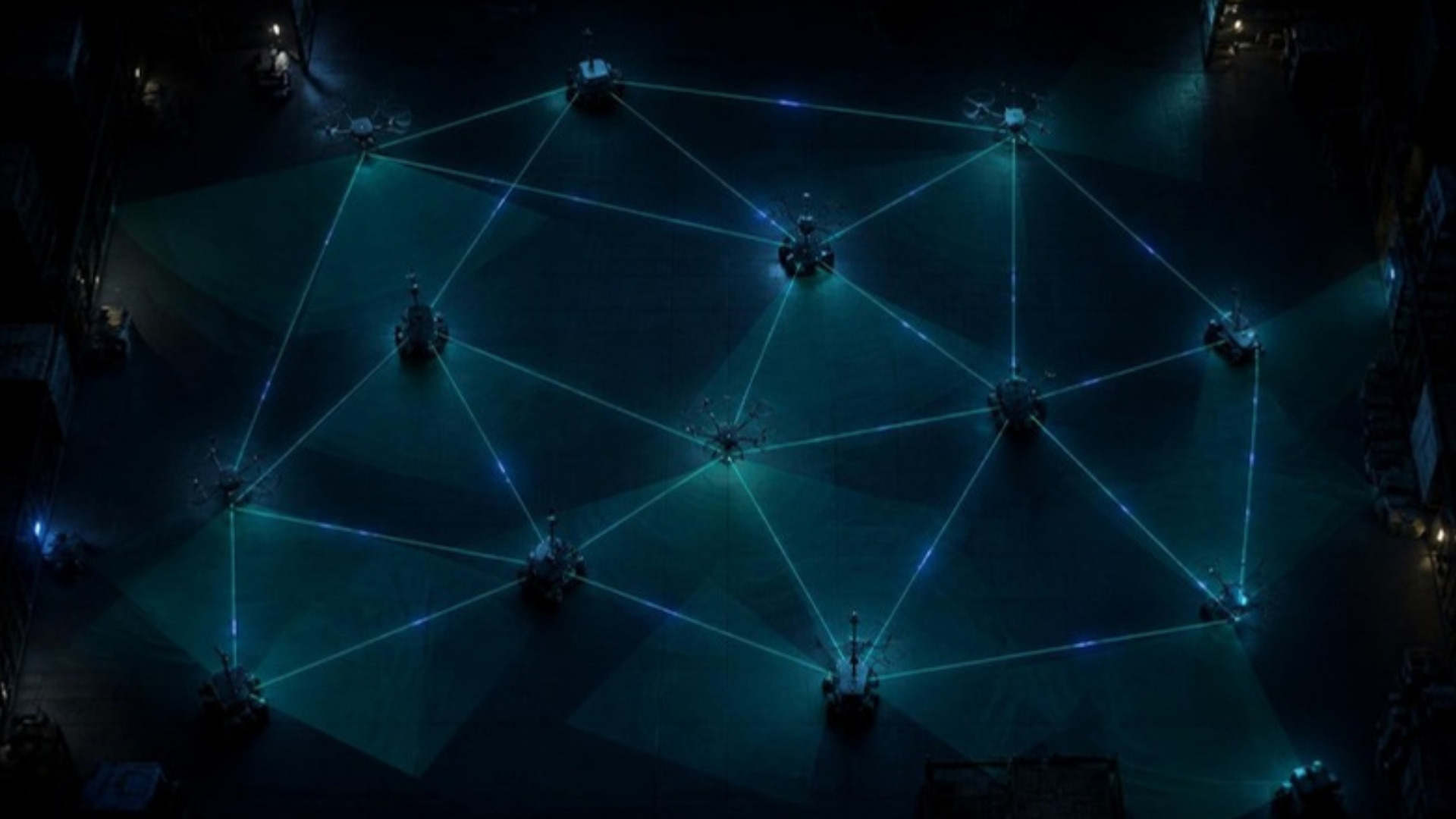 Top-down view of twelve robots on a warehouse floor, linked by a glowing mesh network; their overlapping view cones cover the whole floor